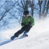 Ein Kind fährt auf Skiern einen Berg hinunter. Es spritzt Schnee hinter ihm auf. 
